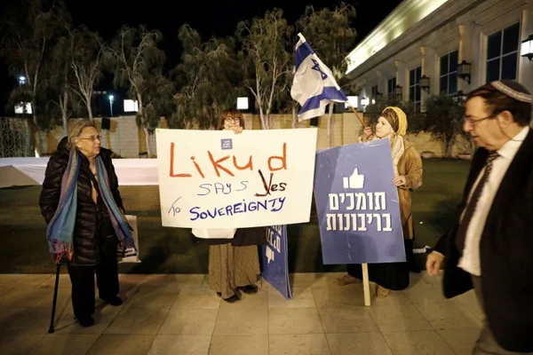 Scène de protestation nocturne où des personnes tiennent des panneaux favorables à la souveraineté, avec un drapeau israélien.
