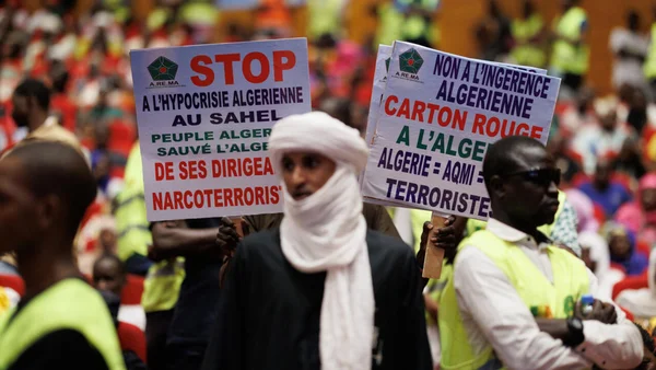 Des personnes protestent avec des panneaux 'Stop à l'hypocrisie algérienne' et 'Non à l'ingérence'.