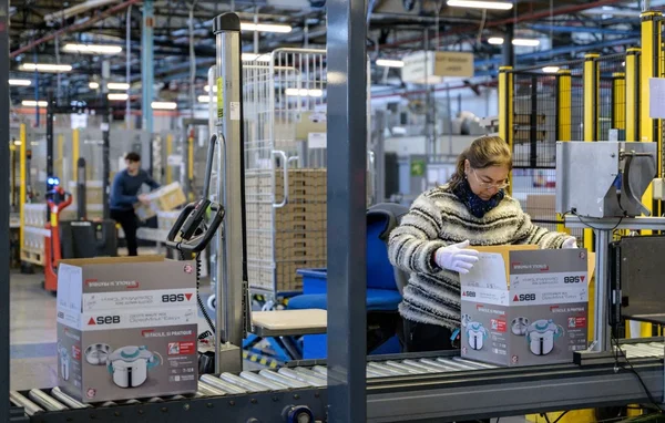 Un ouvrier ganté manipule un carton du Groupe SEB sur un convoyeur dans une usine.