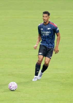 William Saliba, joueur d'Arsenal, debout sur la pelouse avec un ballon à ses pieds.