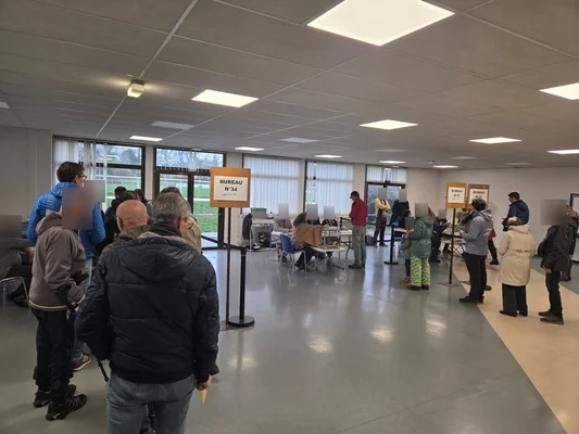 Vue de l'intérieur d'un bureau de vote à Annecy avec des files devant les isoloirs.