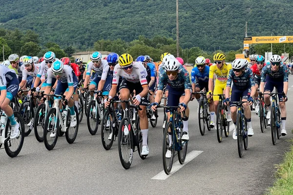 Le peloton du Tour de France sur une route de campagne avec des collines verdoyantes en arrière-plan.