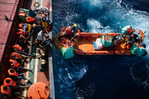 Sauvetage en mer: des sauveteurs transfèrent des migrants en gilets orange d'un canot pneumatique vers un navire.