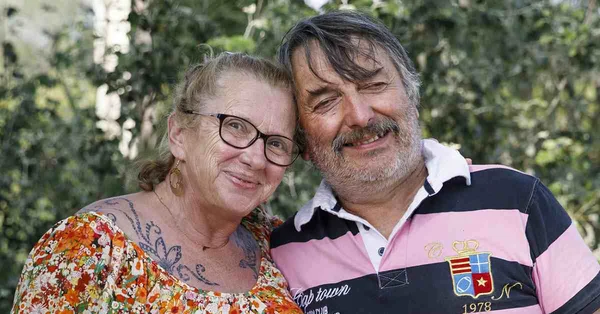 Deux personnes, dont une femme tatouée, posent devant la verdure.