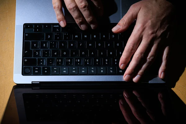 Des mains en train de taper sur le clavier d'un ordinateur portable noir posé sur une table en bois.