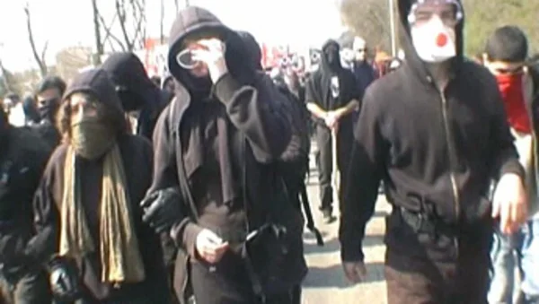 Manifestants en tenue noire et visage dissimulé lors d'un rassemblement en extérieur.