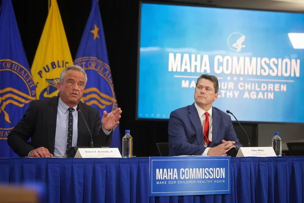 Deux hommes assis à une table avec des micros et le logo 'MAHA COMMISSION' en arrière-plan.