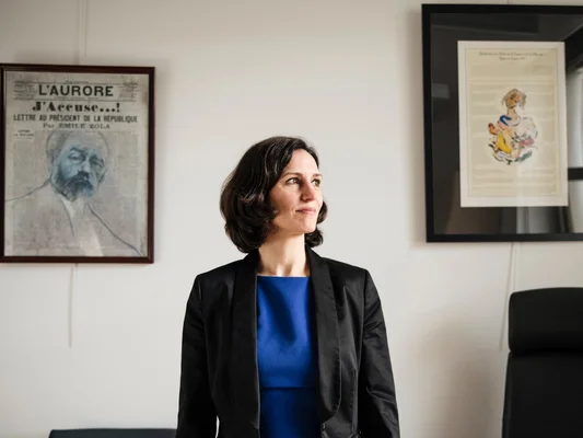 Magali Lafourcade debout devant un mur décoré de cadres et d'une affiche 'J'Accuse'.