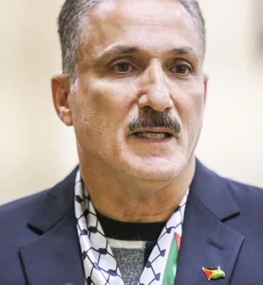 Un homme en costume portant une écharpe à motifs et un pin's lors d'un événement communautaire.