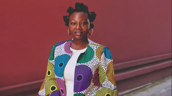 Mirrianne Mahn, auteure d'« Issa », en veste colorée à motifs devant un fond rouge.