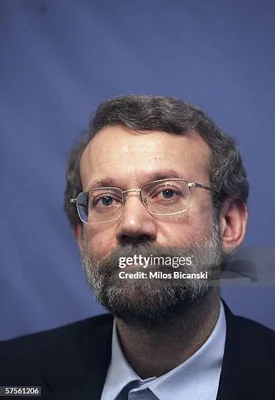 Portrait d'Ali Larijani en costume sombre et chemise bleue devant un fond bleu.
