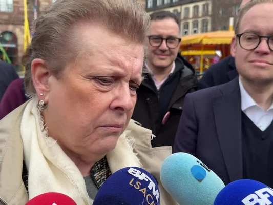 Catherine Trautmann s'adressant aux journalistes devant des microphones en extérieur.