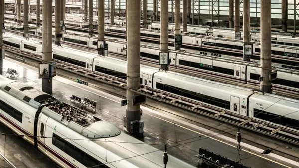 Vue d'une grande gare avec plusieurs trains à grande vitesse blancs garés le long des quais sous des piliers.