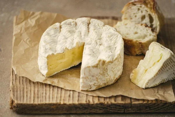 Un camembert entier avec un quartier prélevé, accompagné de pain, sur une planche en bois.