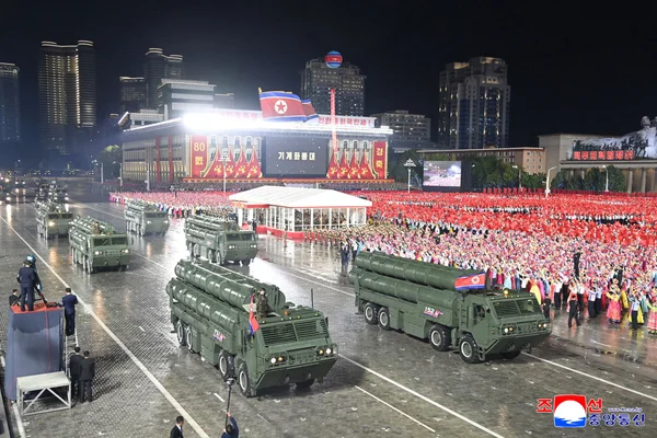 Vue d'ensemble du défilé militaire nocturne à Pyongyang avec les véhicules lanceurs et la foule.