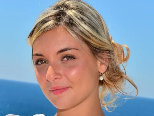 Priscilla Betti portant une boucle d'oreille perle devant un paysage marin.