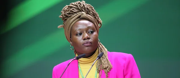 Oratrice en blazer rose et fichu beige devant un podium lors d'un événement littéraire.