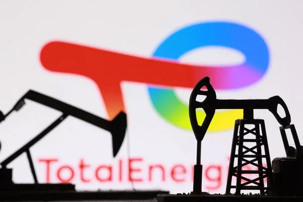 Silhouettes de pompes à pétrole devant le logo TotalEnergies flou en arrière-plan.