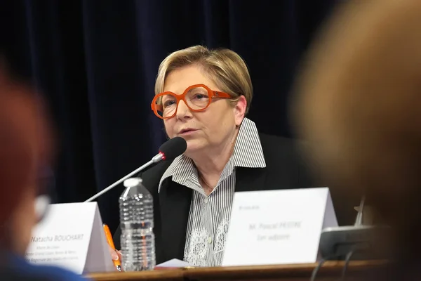 Natacha Bouchart assise devant une table et des micros, en veste noire.