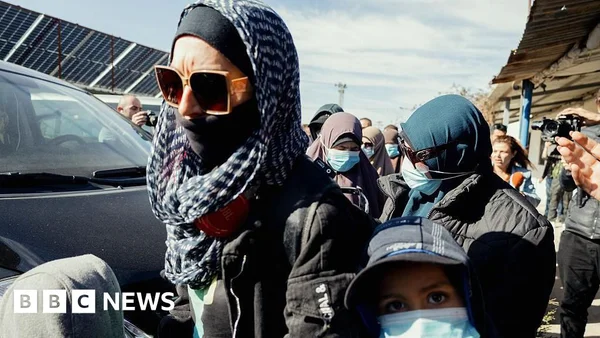 Une personne portant un foulard léger monte dans une fourgonnette noire entourée de photographes.