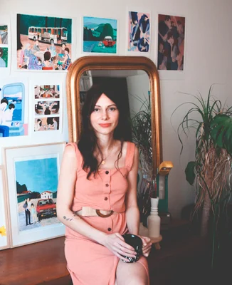 Marie Baudet assise dans son environnement de travail, entourée d'œuvres d'art et de plantes.