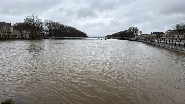 Vue de la Maine en crue à Angers, sous un ciel menaçant, avec les berges inondées.