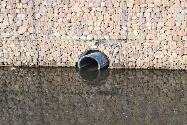 Sortie d'un tuyau d'évacuation avec reflet de l'eau sur un mur de pierres.