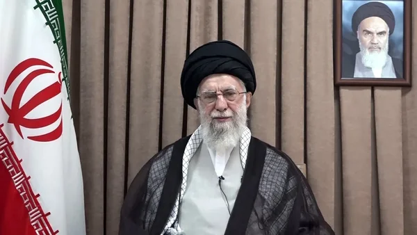 L'Ayatollah Ali Khamenei debout devant un drapeau iranien et un portrait