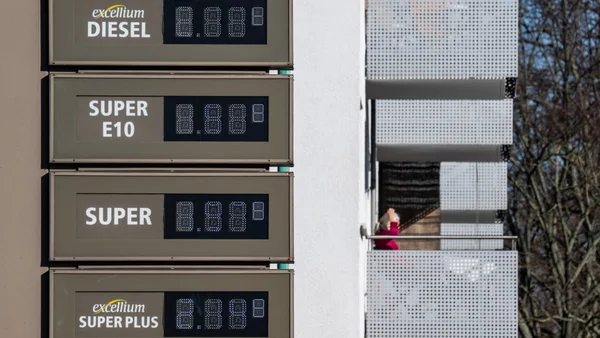 Panneau de tarifs d'une station-service avec un automobiliste à proximité.