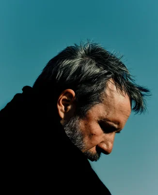 Le réalisateur Denis Villeneuve photographié de profil, le regard pensif, sur fond de ciel bleu.