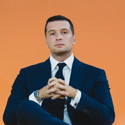 Jordan Bardella lors d'une interview assis sur fond orange.