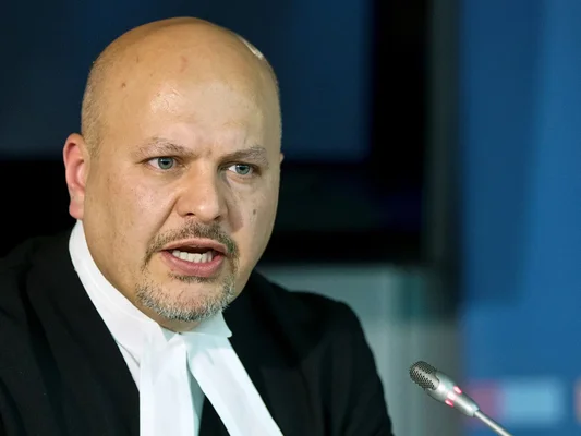 Karim Khan en costume et rabat blanc s'exprimant au micro