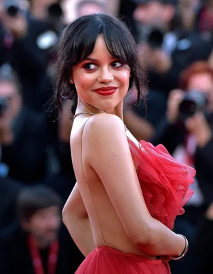 Jenna Ortega posant en robe rouge à volants devant un groupe de photographes.