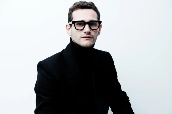 Ulysse Josselin en costume noir et lunettes posant sur fond neutre.
