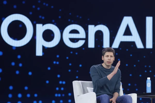 Un conférencier sur scène devant le logo OpenAI, illustrant les ambitions d'achat de puces de l'entreprise.