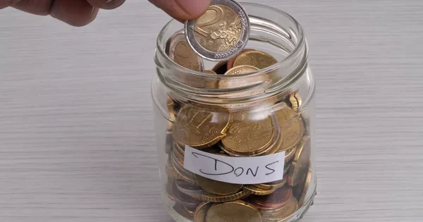 Une pièce de deux euros glissée dans une boîte de dons.