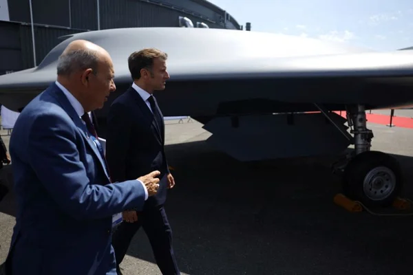 Deux hommes en costume déambulent et discutent devant un avion de chasse lors d'un salon.