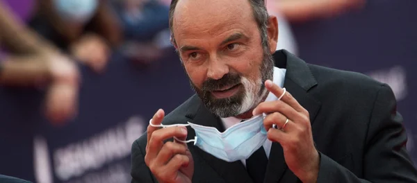 Un homme en costume tenant un masque chirurgical bleu devant lui