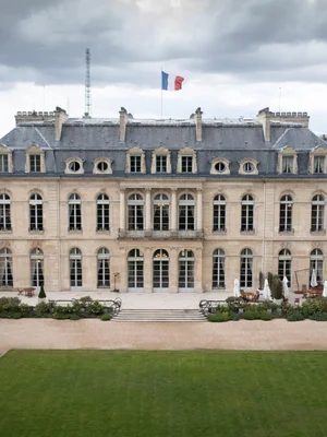 Le palais de l'Élysée sous un temps gris, distingué par son architecture symétrique, ses fenêtres en arc et son drapeau.