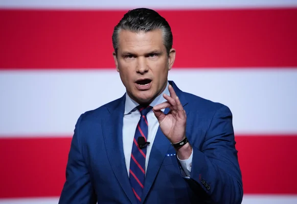 Pete Hegseth s'exprimant publiquement devant un fond aux couleurs américaines, micro en main.