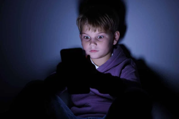 Un enfant utilisant un smartphone dans la pénombre.