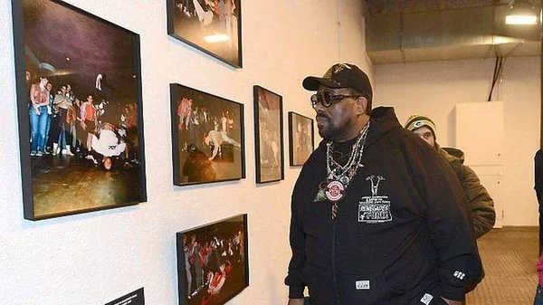 La légende du hip-hop Afrika Bambaataa posant devant une exposition de photographies.