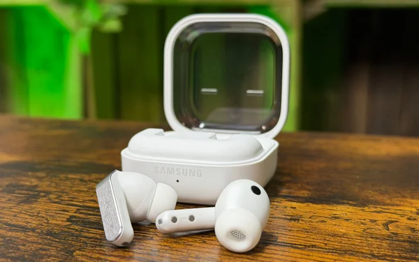 Écouteurs Samsung blancs dans leur étui de charge ouvert, posés sur une surface en bois.