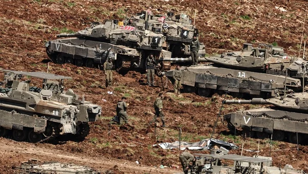 Des militaires se tiennent près de chars et de blindés sur un terrain boueux.