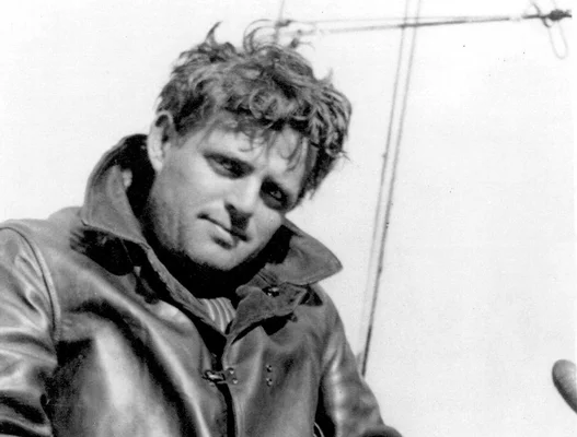 Un homme en veste de cuir posant devant un poteau métallique.