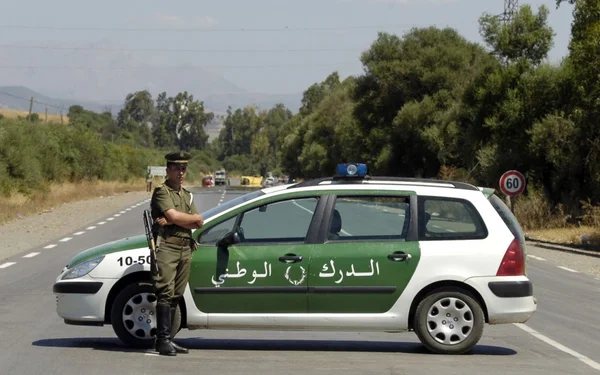 Officier de police à côté d'un véhicule de service sur une route de campagne à Tiaret.