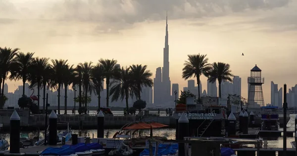 La skyline de Dubaï et la Burj Khalifa visibles depuis une promenade au bord de l'eau, avec des bateaux amarrés au premier plan.