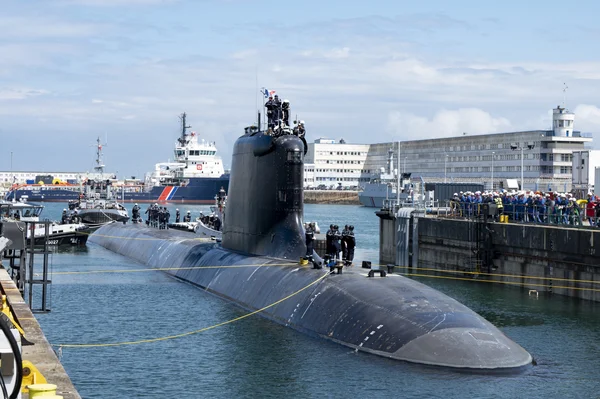 Un sous-marin de type Suffren amarré au port devant des bâtiments industriels, avec l'équipage et des observateurs sur le quai.