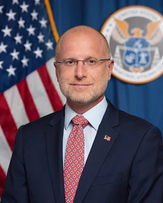 Brendan Carr posant pour un portrait officiel devant les symboles du gouvernement américain.