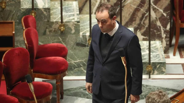 Sébastien Lecornu se tient dans une salle de l'Assemblée, appuyé sur une béquille, après le rejet des motions de censure.